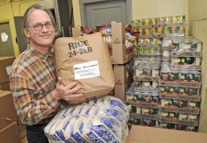 All Faiths Pantry founder smiles poses holding a 25 pound bag of rice in the All Faiths Pantry warehouse.