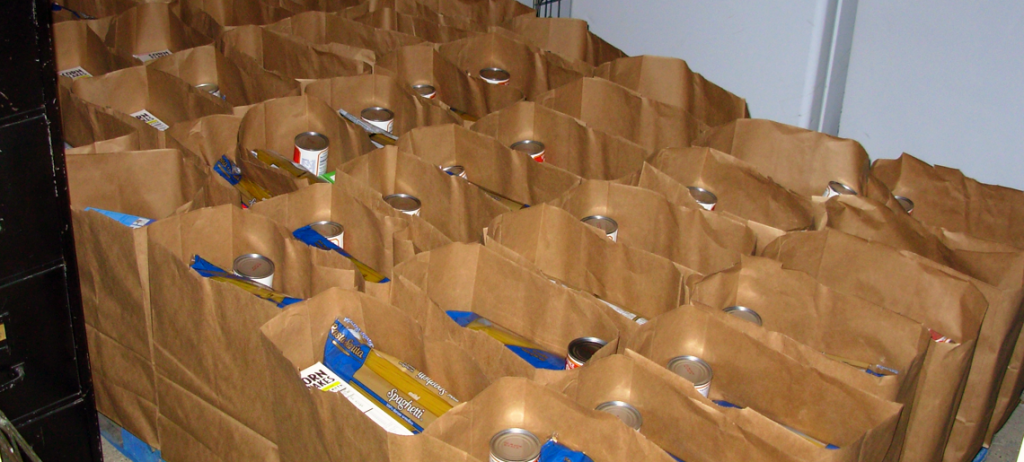Dozens of brown paper bags filled with nonperishable food sit in neat rows on a table.